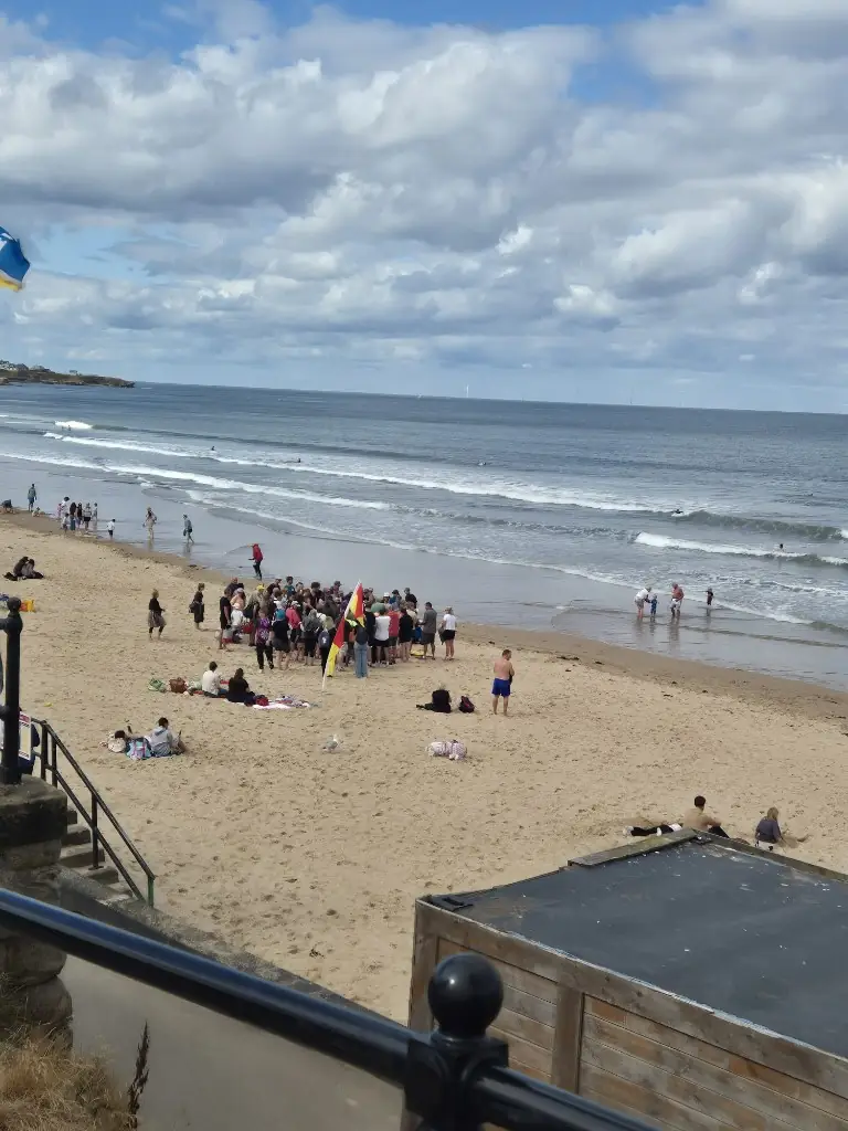 Large group of volunteers gathered on the sand beside a red and yellow flag