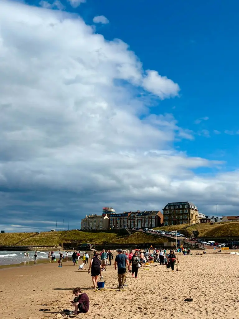 Busy beach cleanup with volunteers, bags and buckets under a dramatic sky
