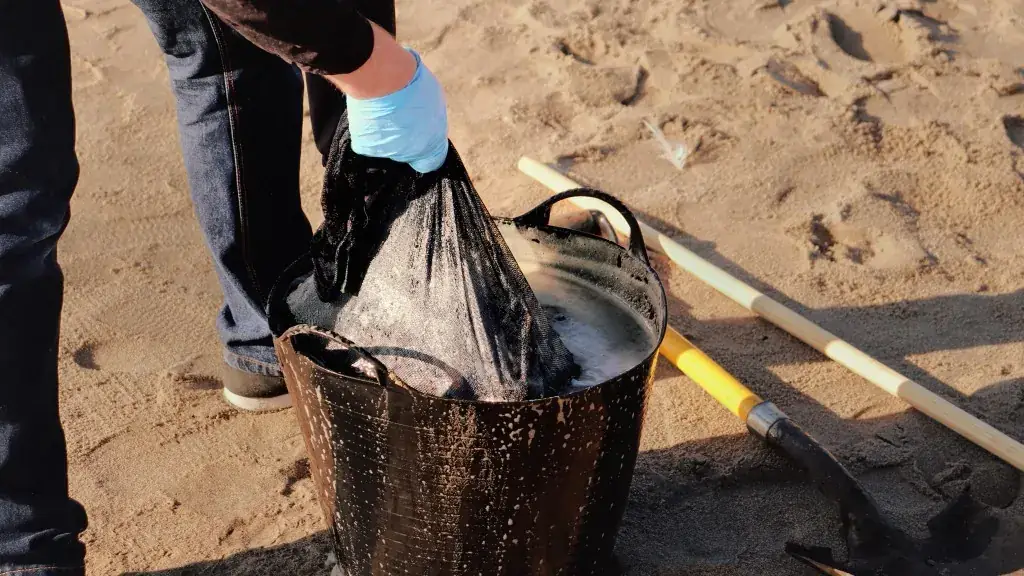 Volunteer lifting a mesh bag from a water-filled bucket beside a shovel