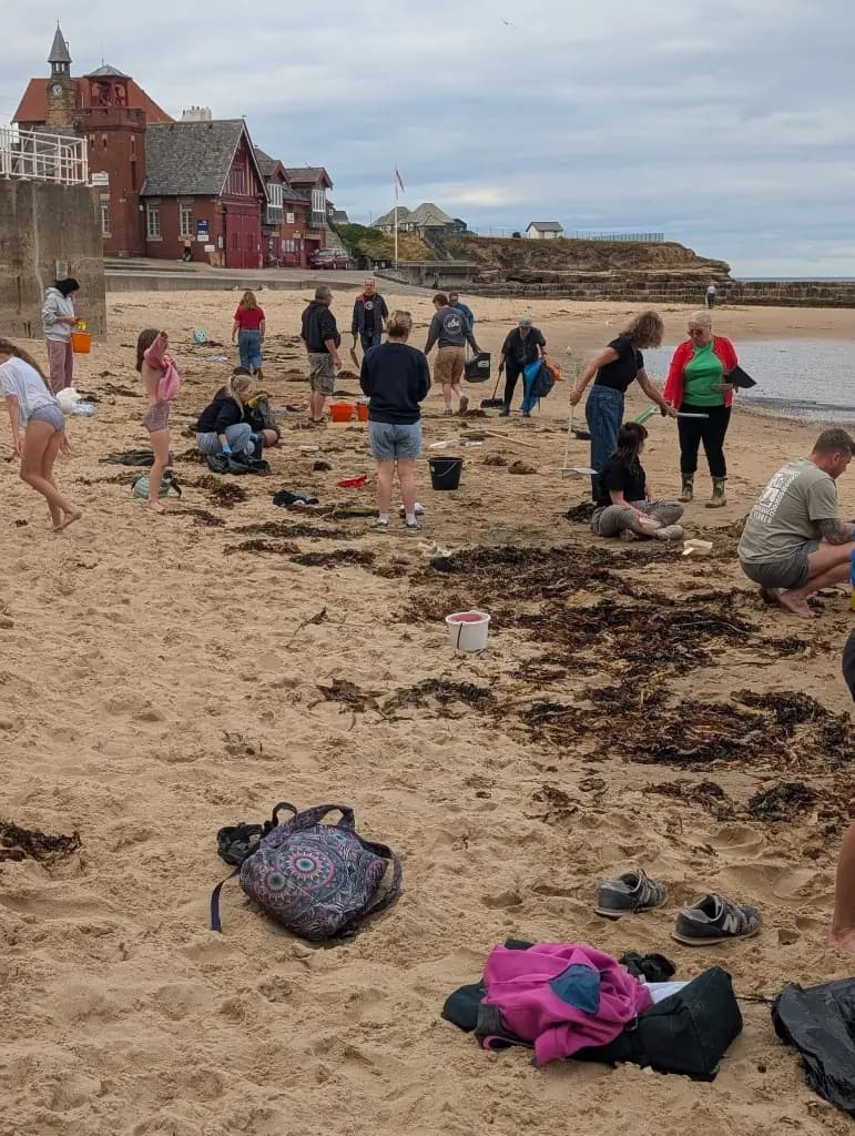 Volunteers with bags and buckets cleaning near the RNLI clock tower building