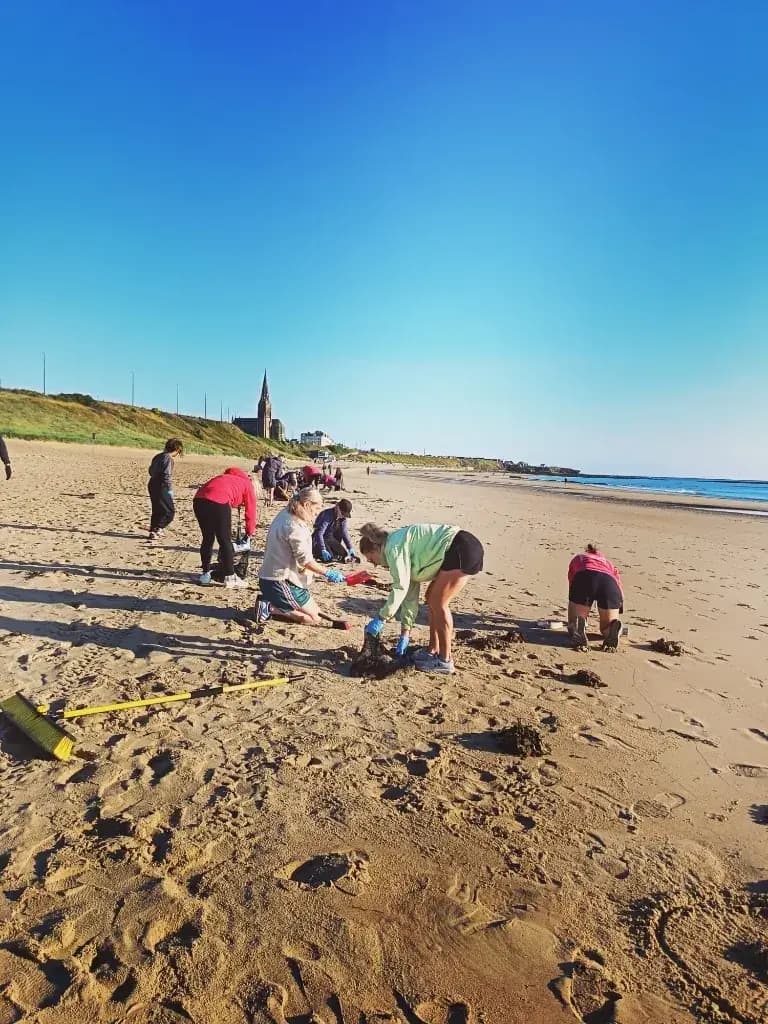 Volunteers cleaning Longsands Beach with a yellow broom in the foreground and St George's Church behind