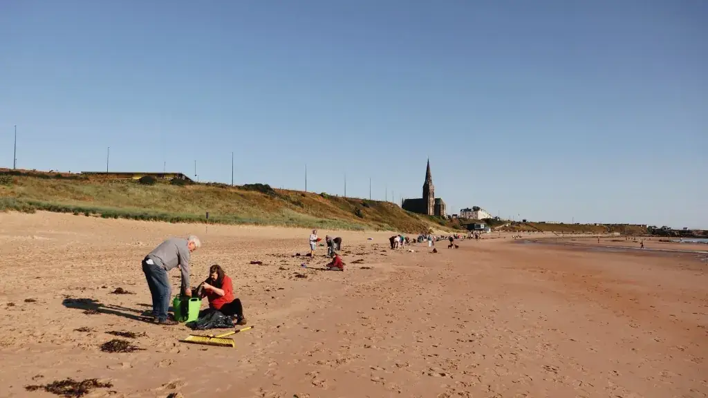 Volunteers with a green bucket and yellow broom on the beach near Cullercoats